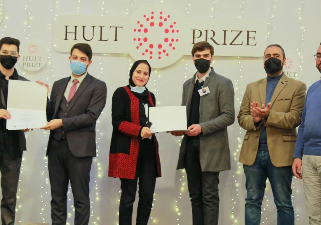 Saja Redwan posing with two other groups of people. Each group is holding an award under a sign that reads 'Hult Prize'.